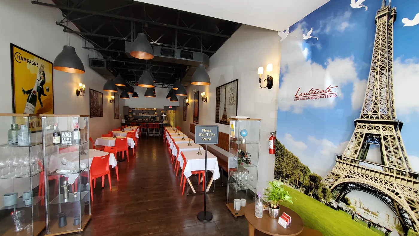 Inside Lentrecote: the dining room with red chairs, white tablecloths, vintage French posters and the Eiffel Tower mural by the entrance
